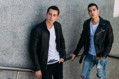 beklenti seksi poz korkuluk yakınındaki mans. çekici bir genç adamın bir siyah deri ceket, beyaz bir T-shirt ve beyaz spor ayakkabı korkuluk yakın duruyor. dostluk. iki model. Giysi gösterilen