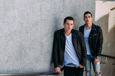 beklenti seksi poz korkuluk yakınındaki mans. çekici bir genç adamın bir siyah deri ceket, beyaz bir T-shirt ve beyaz spor ayakkabı korkuluk yakın duruyor. dostluk. iki model. Giysi gösterilen