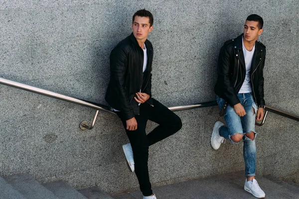 beklenti seksi poz korkuluk yakınındaki mans. çekici bir genç adamın bir siyah deri ceket, beyaz bir T-shirt ve beyaz spor ayakkabı korkuluk yakın duruyor. dostluk. iki model. Giysi gösterilen