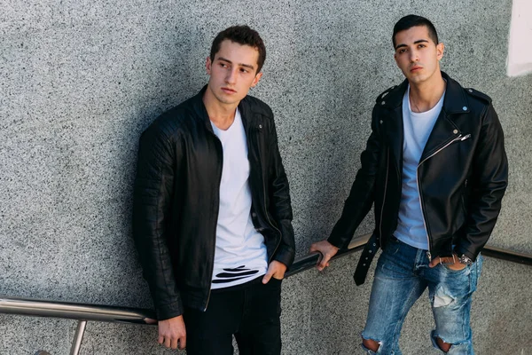 beklenti seksi poz korkuluk yakınındaki mans. çekici bir genç adamın bir siyah deri ceket, beyaz bir T-shirt ve beyaz spor ayakkabı korkuluk yakın duruyor. dostluk. iki model. Giysi gösterilen