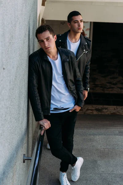 beklenti seksi poz korkuluk yakınındaki mans. çekici bir genç adamın bir siyah deri ceket, beyaz bir T-shirt ve beyaz spor ayakkabı korkuluk yakın duruyor. dostluk. iki model. Giysi gösterilen