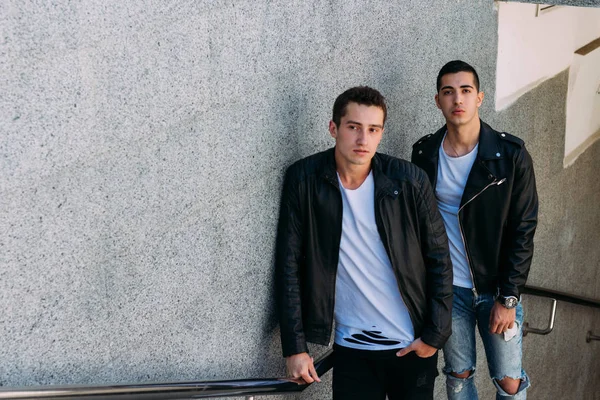 beklenti seksi poz korkuluk yakınındaki mans. çekici bir genç adamın bir siyah deri ceket, beyaz bir T-shirt ve beyaz spor ayakkabı korkuluk yakın duruyor. dostluk. iki model. Giysi gösterilen