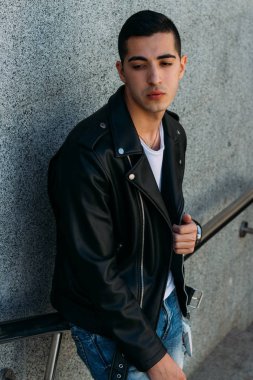 beklenti seksi adam korkuluk yakınındaki poz. çekici bir genç adam bir siyah deri ceket, beyaz gömlek ve Beyaz Ayakkabı yakınındaki korkuluk duruyor.