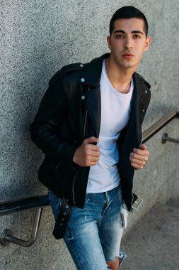 beklenti seksi adam korkuluk yakınındaki poz. çekici bir genç adam bir siyah deri ceket, beyaz gömlek ve Beyaz Ayakkabı yakınındaki korkuluk duruyor.