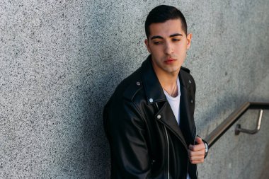 beklenti seksi adam korkuluk yakınındaki poz. çekici bir genç adam bir siyah deri ceket, beyaz gömlek ve Beyaz Ayakkabı yakınındaki korkuluk duruyor.