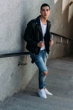 beklenti seksi adam korkuluk yakınındaki poz. çekici bir genç adam bir siyah deri ceket, beyaz gömlek ve Beyaz Ayakkabı yakınındaki korkuluk duruyor.