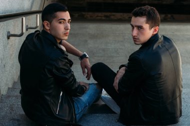 iki adam siyah ceket, kot pantolon ve Beyaz Ayakkabı içinde belgili tanımlık merdiven üstünde oturuyorsun. birde ellerinde. sosyalleşme, Toplantı arkadaşlar.