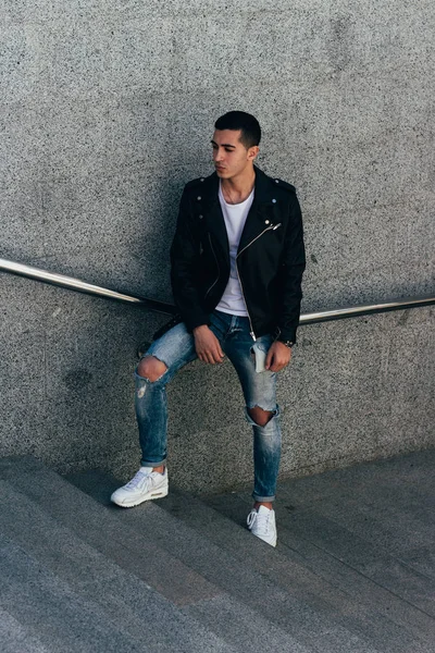 beklenti seksi adam korkuluk yakınındaki poz. çekici bir genç adam bir siyah deri ceket, beyaz gömlek ve Beyaz Ayakkabı yakınındaki korkuluk duruyor.