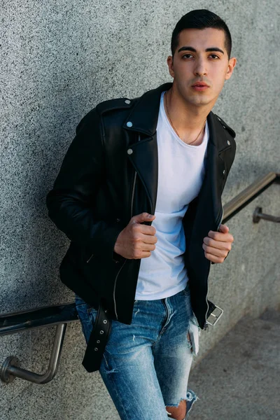 beklenti seksi adam korkuluk yakınındaki poz. çekici bir genç adam bir siyah deri ceket, beyaz gömlek ve Beyaz Ayakkabı yakınındaki korkuluk duruyor.