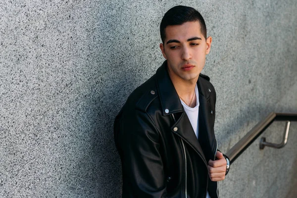 beklenti seksi adam korkuluk yakınındaki poz. çekici bir genç adam bir siyah deri ceket, beyaz gömlek ve Beyaz Ayakkabı yakınındaki korkuluk duruyor.