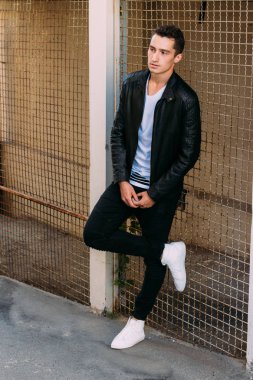 güzel ve çekici adam şehir kılavuzunda yakın duran, poz. siyah deri kurta, beyaz T-shirt, kot pantolon ve beyaz ayakkabı giymiş.