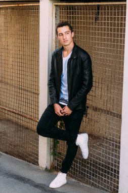 güzel ve çekici adam şehir kılavuzunda yakın duran, poz. siyah deri kurta, beyaz T-shirt, kot pantolon ve beyaz ayakkabı giymiş.