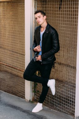 güzel ve çekici adam şehir kılavuzunda yakın duran, poz. siyah deri kurta, beyaz T-shirt, kot pantolon ve beyaz ayakkabı giymiş.