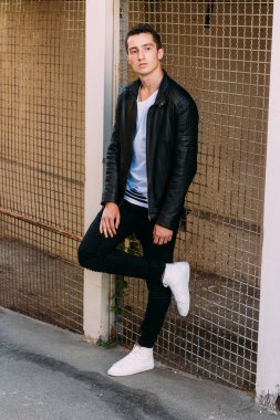 güzel ve çekici adam şehir kılavuzunda yakın duran, poz. siyah deri kurta, beyaz T-shirt, kot pantolon ve beyaz ayakkabı giymiş.