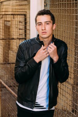 güzel ve çekici adam şehir kılavuzunda yakın duran, poz. siyah deri kurta, beyaz T-shirt, kot pantolon ve beyaz ayakkabı giymiş.