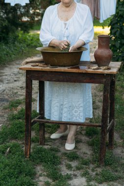 Yaşlı bir kadın bahçede giysi yıkama. Beyaz vintage giyim. Taşra hayatı. elbise bir ip üzerinde kurur. Masanın yanındaki clothespins vardır. Stark'ın eski bir bakır lavabo ve kil sürahi.