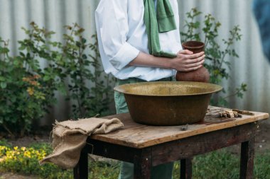 beyaz bir gömlek ve yeşil kazak, çocukta bir kil sürahi tutar, suyun dışında bakır lavabo içine dökülen. Yardım, kırsal. Köyü.