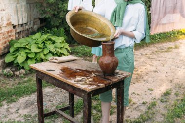 beyaz bir gömlek ve yeşil kazak, çocukta bir kil sürahi tutar, suyun dışında bakır lavabo içine dökülen. Yardım, kırsal. Köyü.