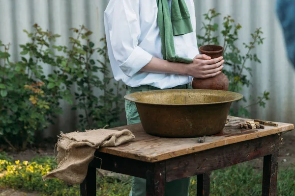 beyaz bir gömlek ve yeşil kazak, çocukta bir kil sürahi tutar, suyun dışında bakır lavabo içine dökülen. Yardım, kırsal. Köyü.