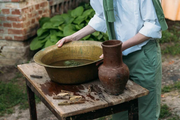 beyaz bir gömlek ve yeşil kazak, çocukta bir kil sürahi tutar, suyun dışında bakır lavabo içine dökülen. Yardım, kırsal. Köyü.