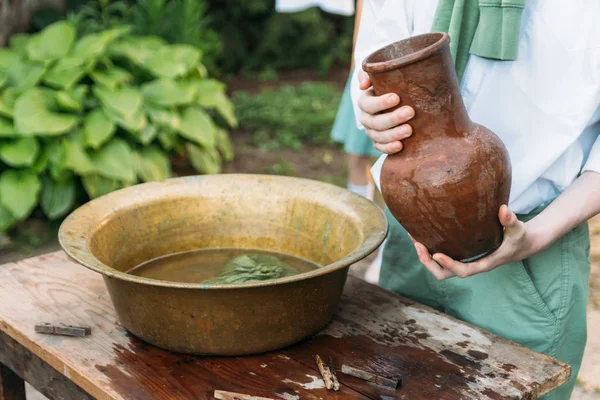 beyaz bir gömlek ve yeşil kazak, çocukta bir kil sürahi tutar, suyun dışında bakır lavabo içine dökülen. Yardım, kırsal. Köyü.