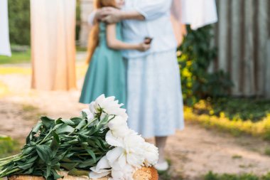 güdük üzerinde beyaz peonies bir buket var. arka plan, Büyükanne, yaşlı bir kadın beyaz, vintage giyim duruyor ve onun torunu, Yeşil elbiseli bir kız bahçede sarılarak. Toplantı ve tebrik ederim, bir hediye