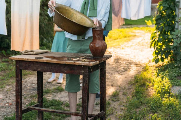 beyaz bir gömlek ve yeşil kazak, çocukta bir kil sürahi tutar, suyun dışında bakır lavabo içine dökülen. Yardım, kırsal. Köyü.