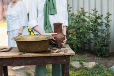 beyaz bir gömlek ve yeşil kazak, çocukta bir kil sürahi tutar, suyun dışında bakır lavabo içine dökülen. Yardım, kırsal. köy. arka planda yaşlı bir kadın olduğunu