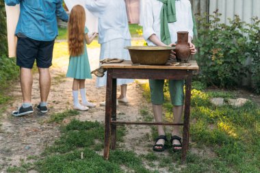beyaz bir gömlek ve yeşil kazak, çocukta bir kil sürahi tutar, suyun dışında bakır lavabo içine dökülen. Yardım, kırsal. köy. arka planda bir kız ve bir erkek yaşlı bir kadın olduğunu, yıkanmış Çamaşırhane asıyorlar