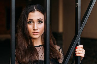 Genç, güzel bir kız portresi. Siyah elbiseli esmer siyah çubuklar ile kafes yakın duruyor. Onlara veriyor. Genç ve güzel kadın moda şık portresi duygusal portresi. Şehir portre. üzgün kız. esmer siyah elbise zekâ