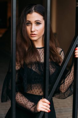 Genç, güzel bir kız portresi. Siyah elbiseli esmer siyah çubuklar ile kafes yakın duruyor. Onlara veriyor. Genç ve güzel kadın moda şık portresi duygusal portresi. Şehir portre. üzgün kız. esmer siyah elbise zekâ