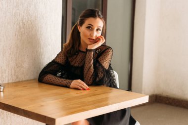 güzel esmer beyaz sandalye ahşap bir masada oturan. bir panel ve bir yıldız ile siyah bir elbise öyle. bir toplantı için bekliyor. Konumlandırma. Kadın portre. Cafe City