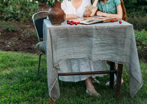 Büyükanne torunu ile masada oturur, onun gençlik fotoğrafları ile eski bir albüm onu gösteriyor. bir kil vazo çiçek ve kiraz ile geçerli. Aile öyküleri ve anılar. Yaşlı kadın vintage gelinlik ve kız giymiş ben