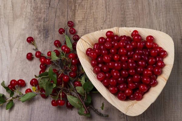 fresh red cherries in a wooden plate on a wooden table. wooden plate on a wooden background. next to it is a cherry branch with cherries and green leaves.a plate in the form of a triangle. ecology. proper nutrition.
