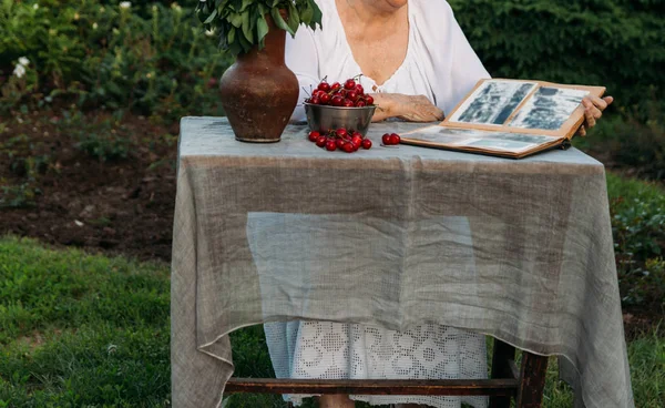 Memories of the elderly. visit grandmother. grandmother sitting in a chair in the garden and watching an old album with photos, recounts and remembers the familys story. — Stock Photo, Image