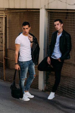 güzel ve çekici adam şehirde ayakta, poz. siyah deri kurta, beyaz T-shirt, kot pantolon ve beyaz ayakkabı giymiş.