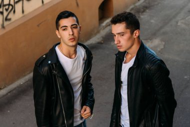 güzel ve çekici adam şehirde ayakta, poz. siyah deri kurta, beyaz T-shirt, kot pantolon ve beyaz ayakkabı giymiş.