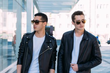 güzel ve çekici adam şehirde ayakta, poz. siyah deri kurta, beyaz T-shirt, kot pantolon ve beyaz ayakkabı giymiş. ayna Binası yakınında. siyah gözlük şehirde dolaşmak. iletişim. Toplantı arkadaşlar.