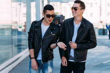 güzel ve çekici adam şehirde ayakta, poz. siyah deri kurta, beyaz T-shirt, kot pantolon ve beyaz ayakkabı giymiş. ayna Binası yakınında. siyah gözlük şehirde dolaşmak. iletişim. Toplantı arkadaşlar.