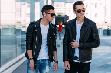 güzel ve çekici adam şehirde ayakta, poz. siyah deri kurta, beyaz T-shirt, kot pantolon ve beyaz ayakkabı giymiş. ayna Binası yakınında. siyah gözlük şehirde dolaşmak. iletişim. Toplantı arkadaşlar.