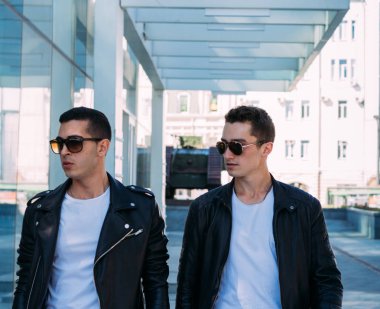 güzel ve çekici adam şehirde ayakta, poz. siyah deri kurta, beyaz T-shirt, kot pantolon ve beyaz ayakkabı giymiş. ayna Binası yakınında. siyah gözlük şehirde dolaşmak. iletişim. Toplantı arkadaşlar.