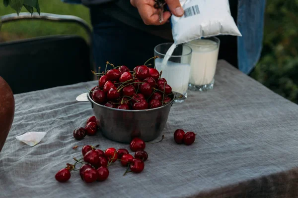 Muž nalévá mléko do sklenice z balíčku. na stole je deska s cherry a vázu s květinami. muž v džínové bundě a s klíči — Stock fotografie