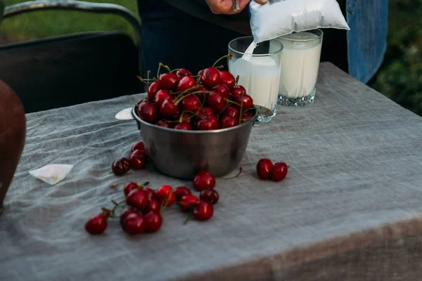 Muž nalévá mléko do sklenice z balíčku. na stole je deska s cherry a vázu s květinami. muž v džínové bundě a s klíči — Stock fotografie