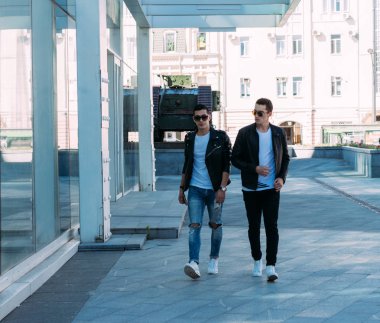 güzel ve çekici adam şehirde oluyor poz. siyah deri kurta, beyaz T-shirt, kot pantolon ve beyaz ayakkabı giymiş. ayna Binası yakınında. siyah gözlük şehirde dolaşmak. iletişim. Toplantı arkadaşlar.