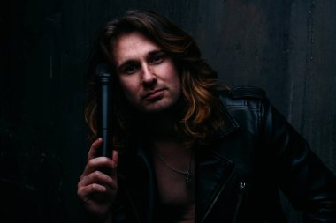 acımasız adam uzun saçlı çıplak bir vücut üzerinde deri ceketli. Yalnız bir adam üzgün ve umutsuz. bir mikrofon elinde tutuyor, duvara eğilir