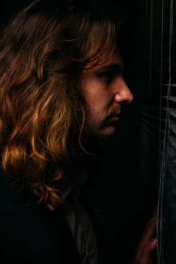 uzun saçlı bir adam güneşlikler loblar, siyah ceketli açılarak pencerenin duruyor. Sokakta insanlar üzerinde casus bakmak gündoğumu. pencereden dışarı bakıp