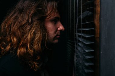 uzun saçlı bir adam güneşlikler loblar, siyah ceketli açılarak pencerenin duruyor. Sokakta insanlar üzerinde casus bakmak gündoğumu. pencereden dışarı bakıp