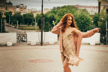 Mutlu kız elbise ve şapka bir şehir sokak ve kamera bakarak gülümsüyordu. bir şapka, bir çiçek ve sıcak renk bir ceket elbise