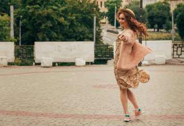 Mutlu kız elbise ve şapka bir şehir sokak ve kamera bakarak gülümsüyordu. bir şapka, bir çiçek ve sıcak renk bir ceket elbise