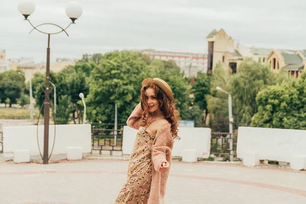 Sorrindo menina feliz em vestido e chapéu em uma rua da cidade e olhando para a câmera. em um chapéu, um vestido em uma flor e uma jaqueta de cores quentes — Fotografia de Stock